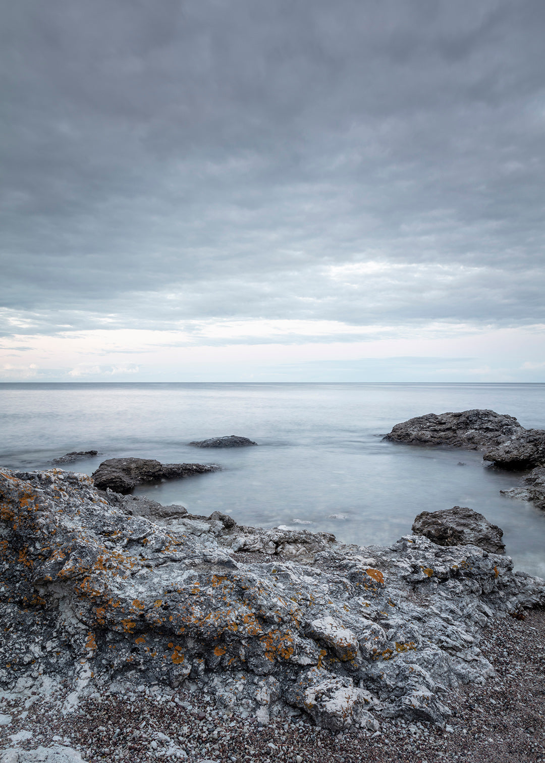Dramatisk klippekyst på Gotland med grå klipper, lav og roligt hav under skydækket himmel.